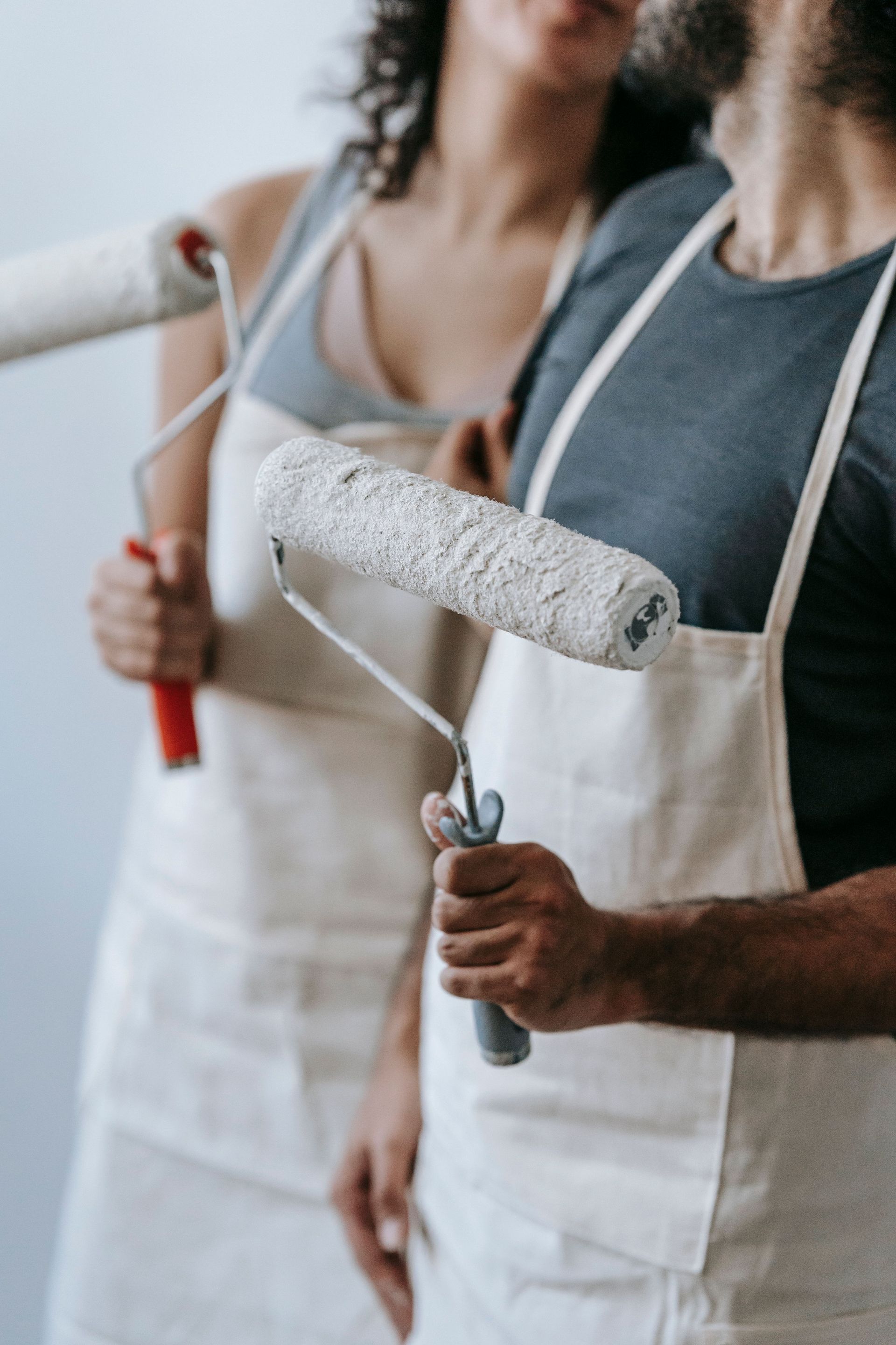 A couple in aprons using paint rollers for home renovation indoors.