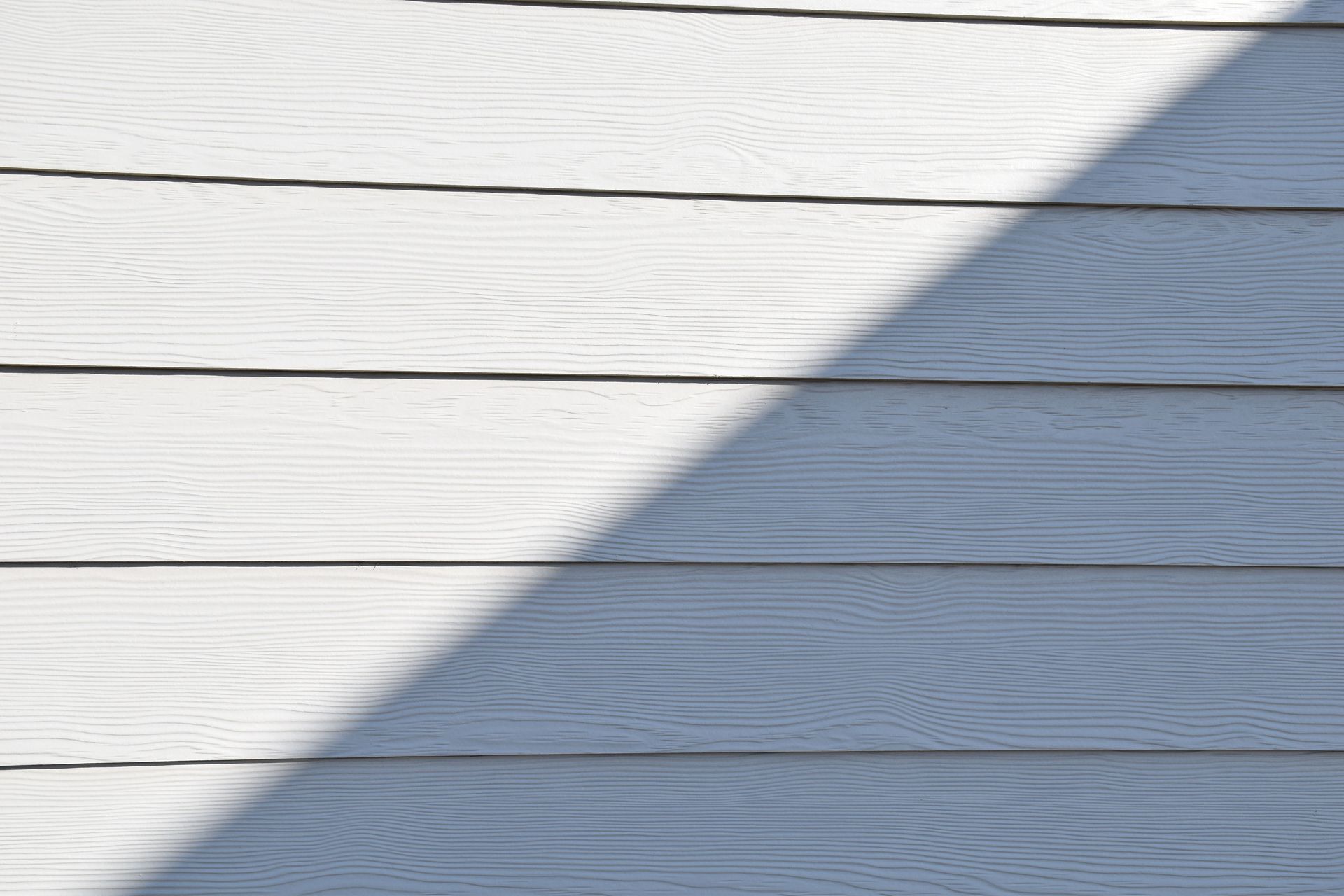 Close-up of a white wooden wall featuring a bold diagonal shadow.